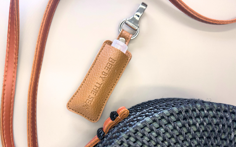Almond Lip Balm displayed with a sling handbag against a plain wall background.